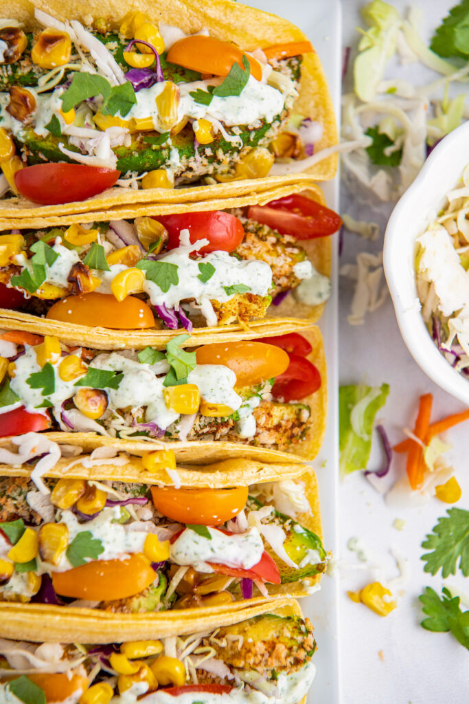 Tacos on white plate stuffed with avocados, corn, tomatoes, sliced cabbage and crema