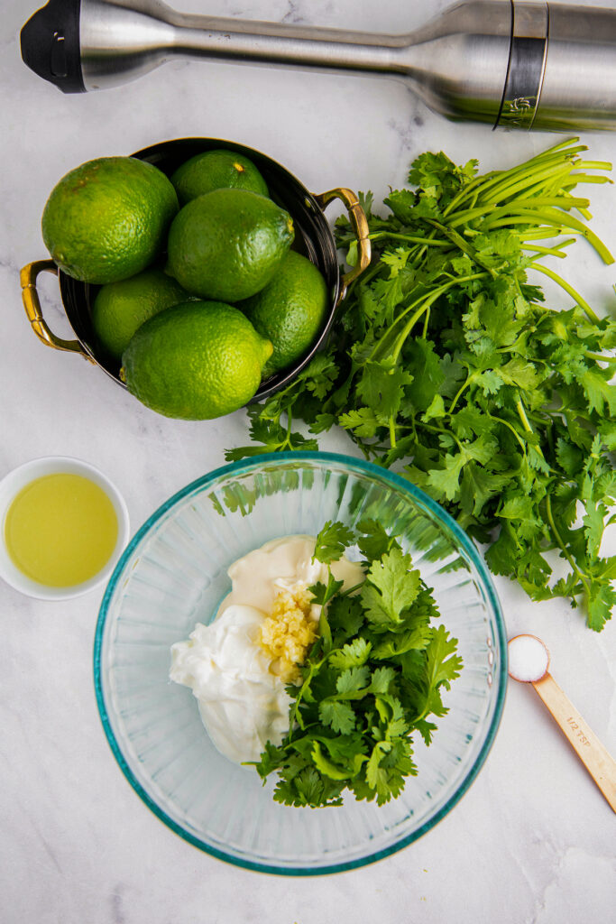 In a glass bowl sour cream, mayonnaise, cilantro and garlic. On the side a measuring spoon with salt, lime juice and cilantro