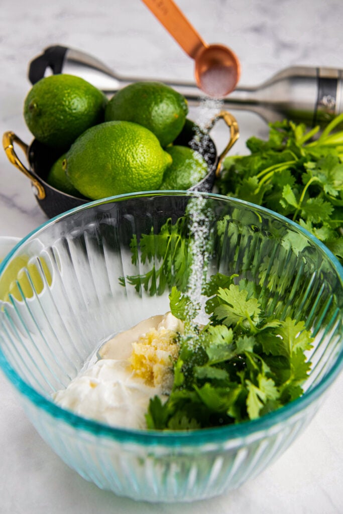 A glass bowl with cilantro, sour cream, mayonnaise, garlic and salt poured into bowl