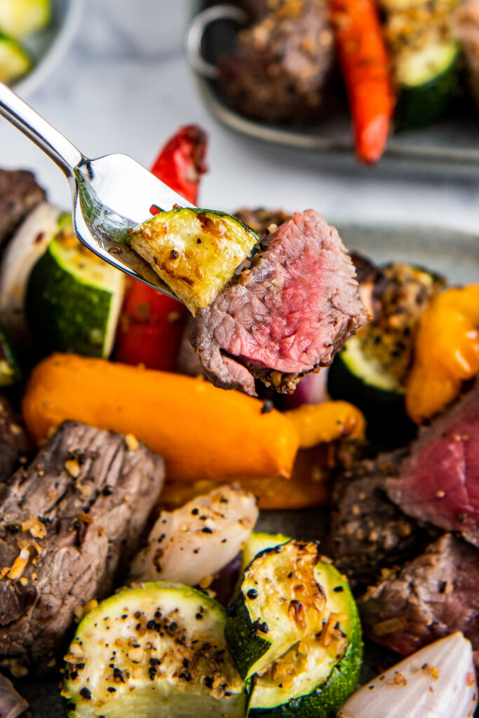 A for with steak and zucchini above a plate with steak, peppers, zucchini and onions.