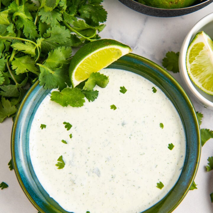 Green bowl filled with cilantro lime crema and fresh cilantro and lime on the side