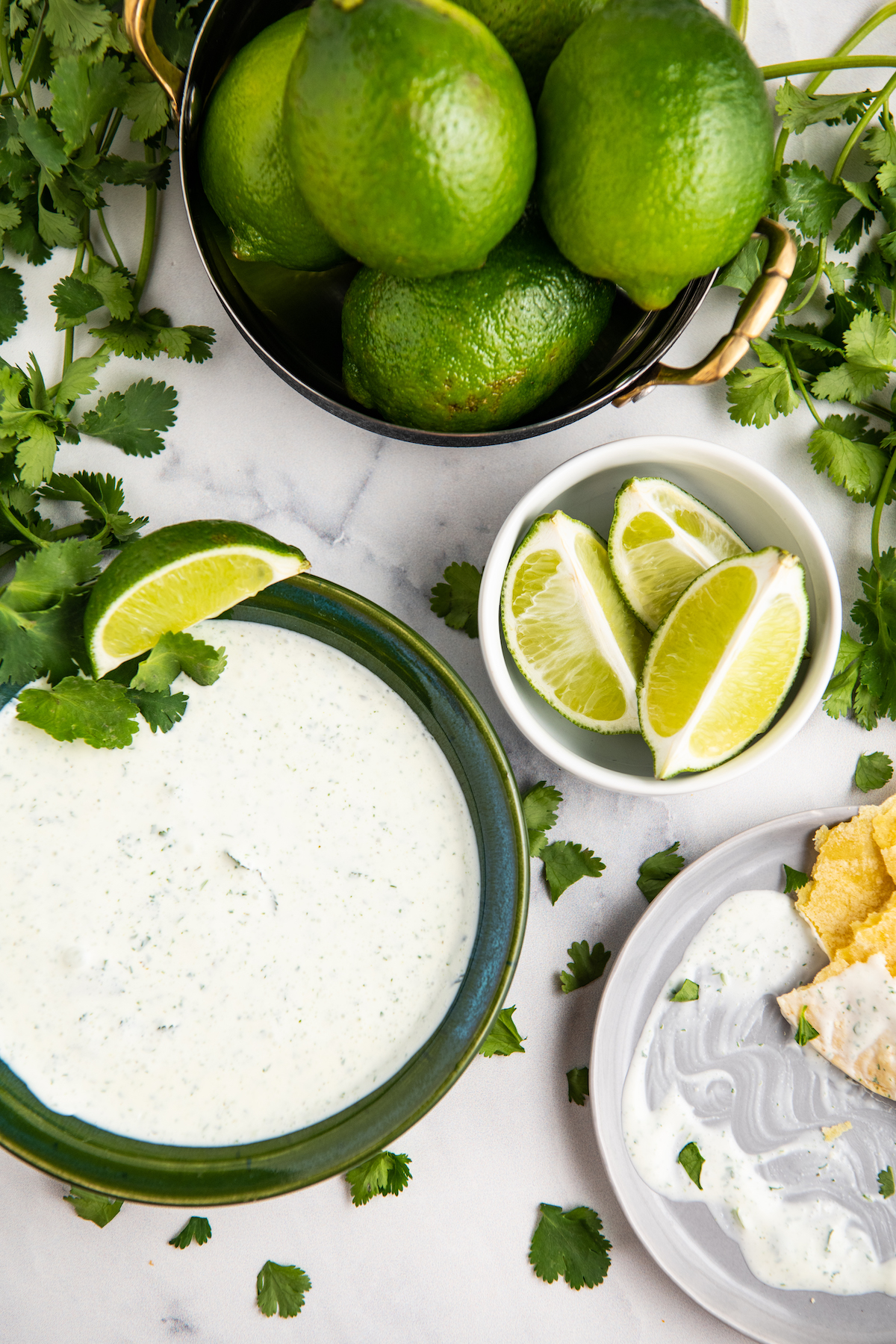 Cilantro Lime Crema in a green bowl with a spoon and cilantro and lime as garnish