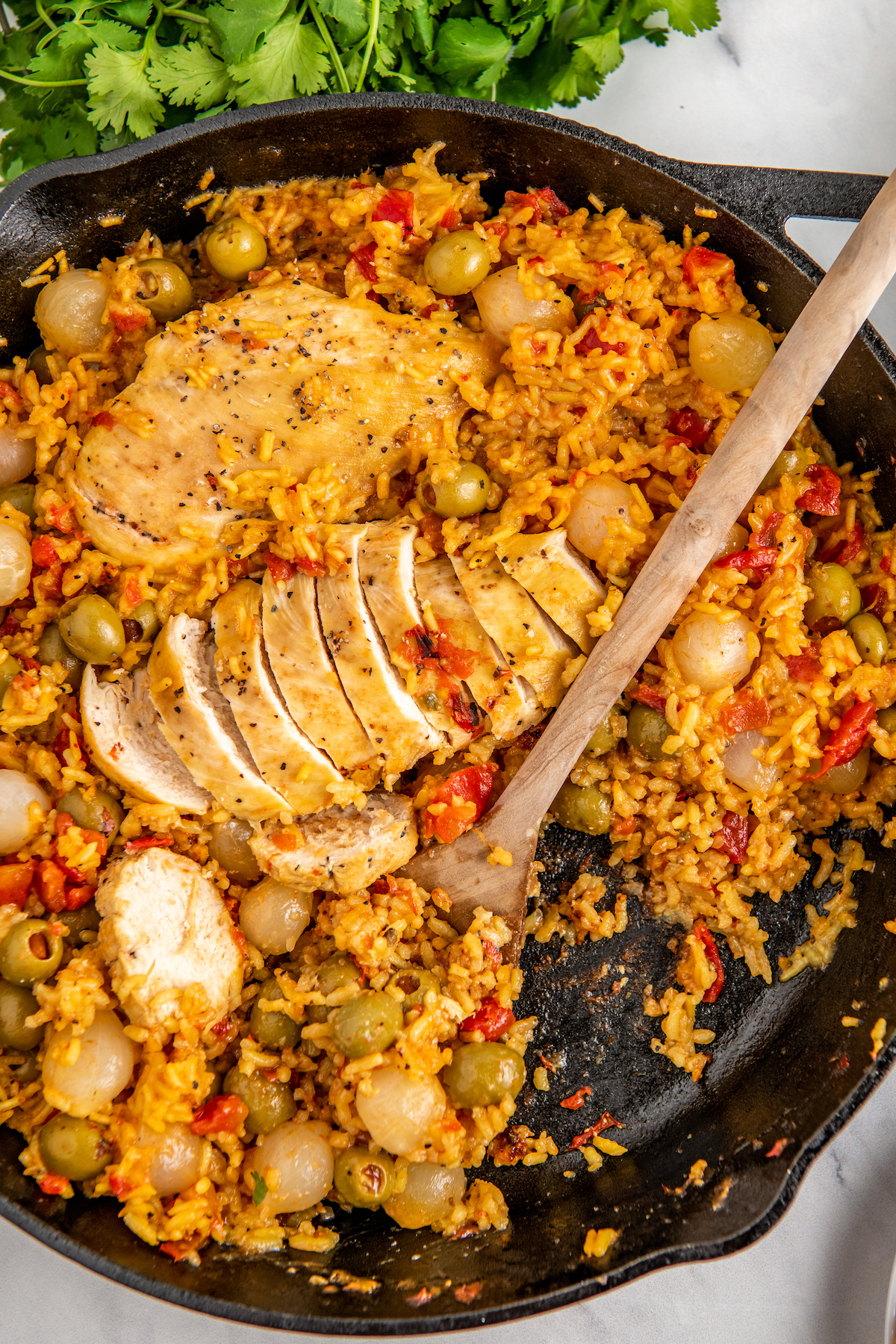 Cast iron skillet with Spanish chicken and rice and a wooden serving spoon