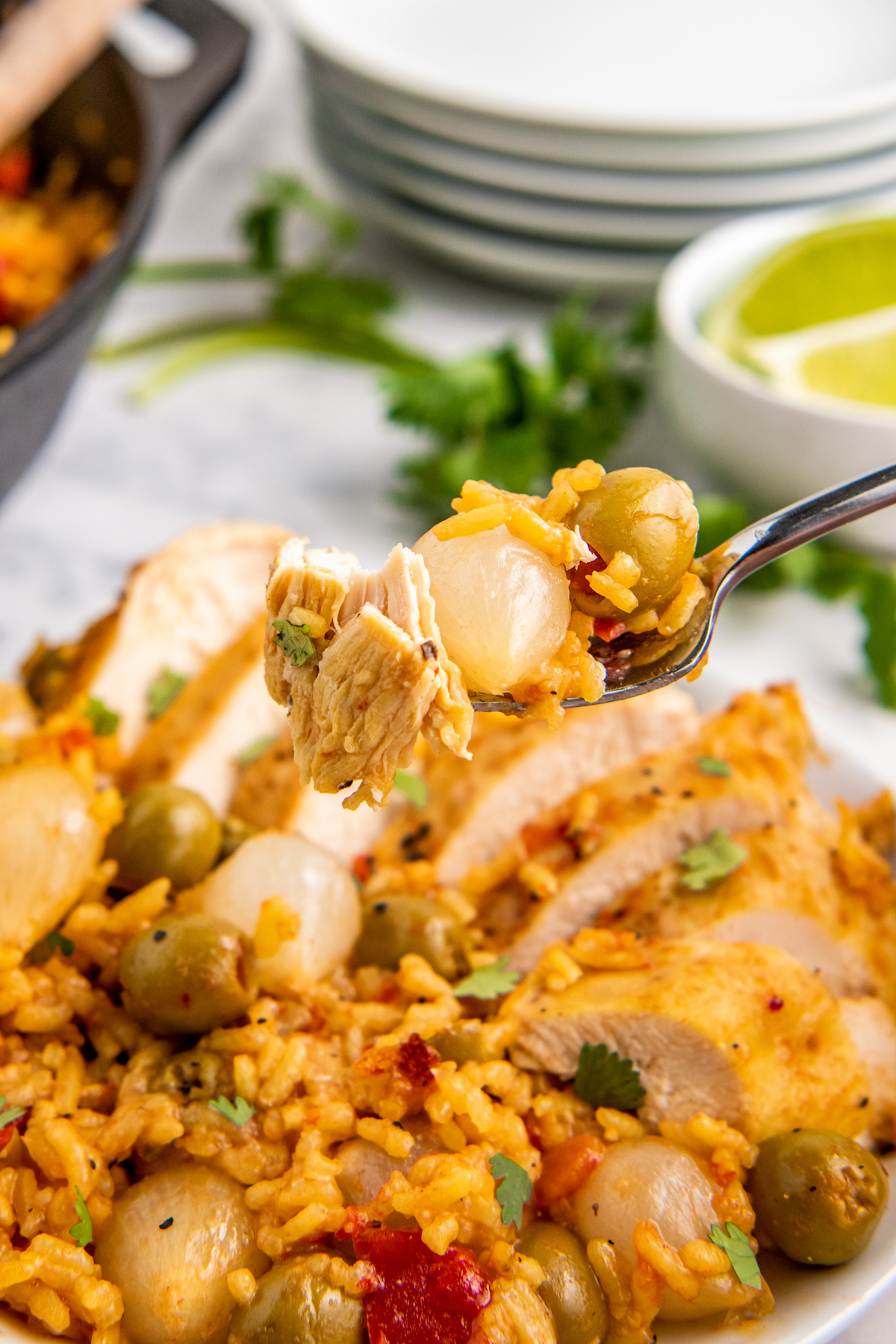 A fork with Spanish chicken and rice, olive and onion over a plate with more chicken and rice
