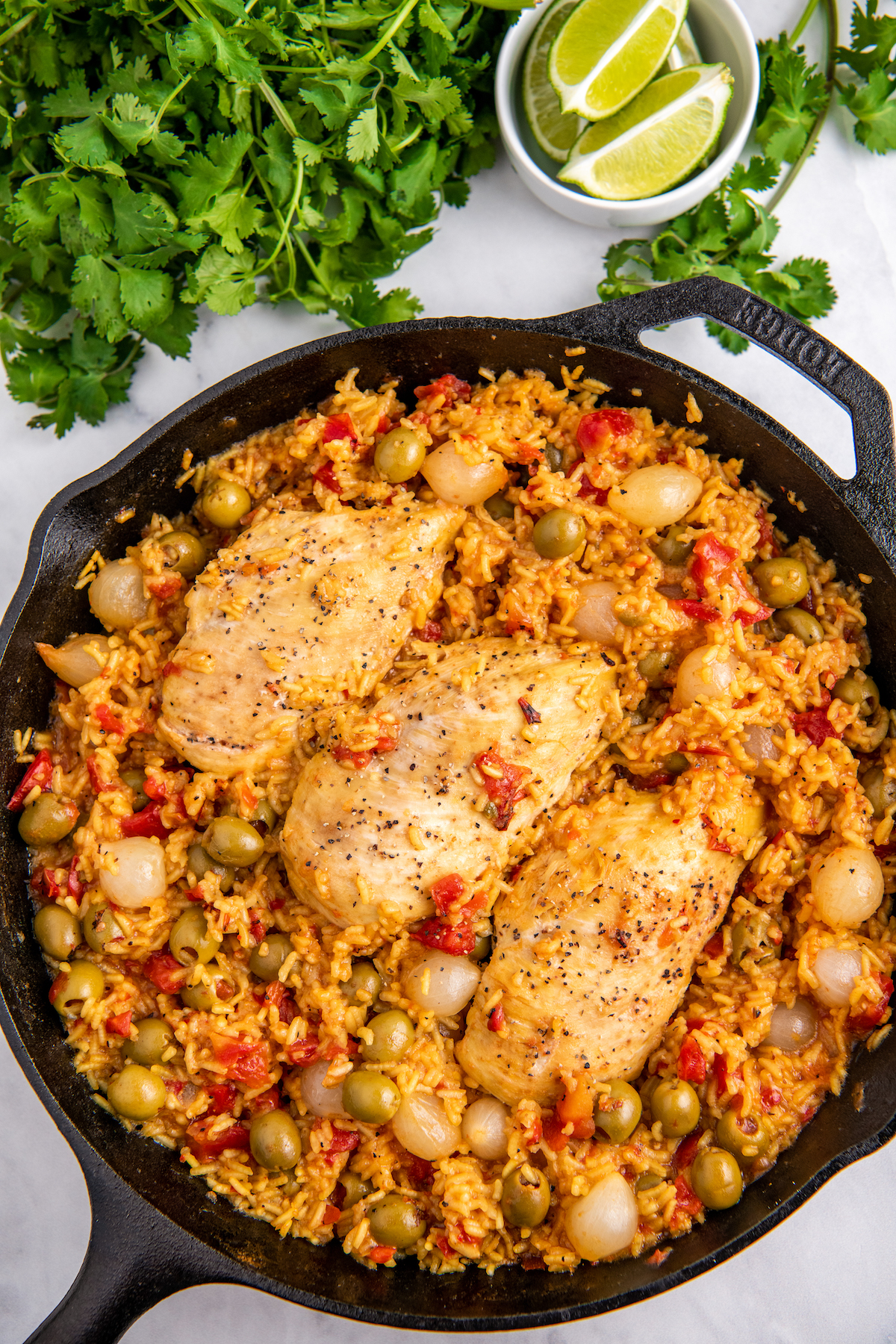 Cast iron skillet with Spanish rice and chicken. the rice has olives and onions in it and parsley on the side