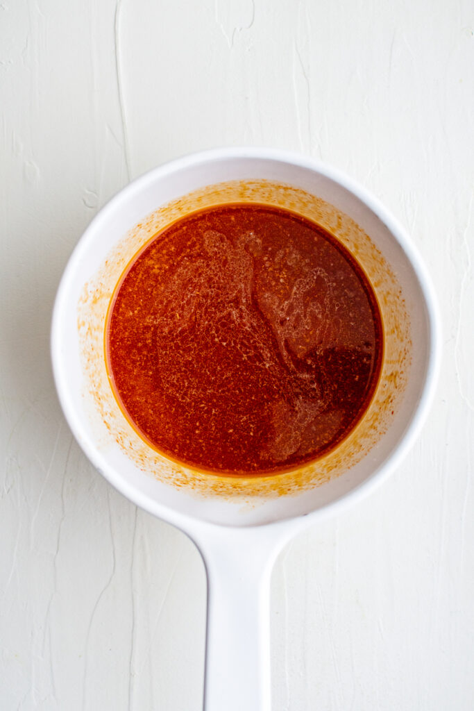 A cup of honey has turned red from the cayenne pepper.