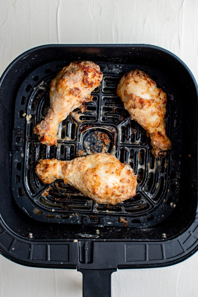 Three chicken legs are placed in the basket of an air fryer. 
