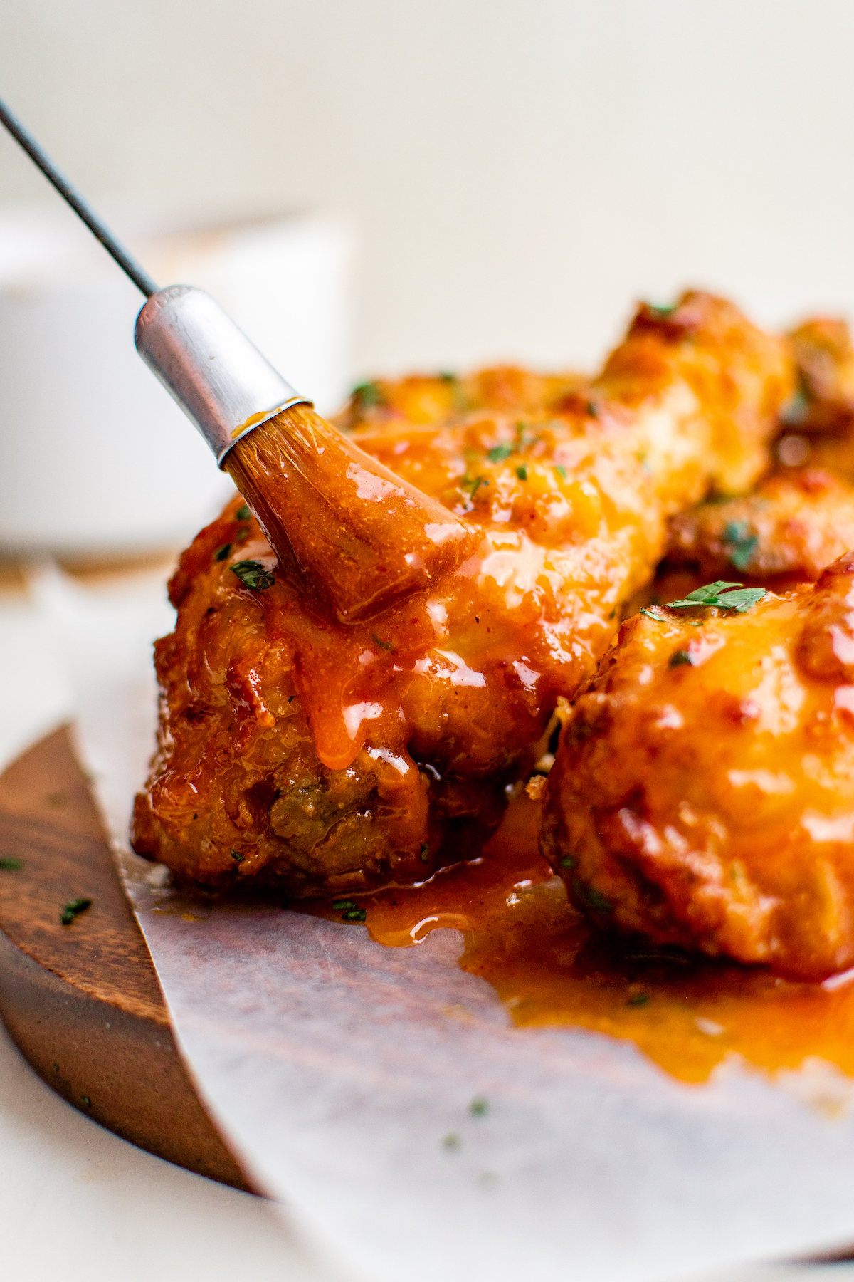 Up close image of fried chicken legs being brushed with hot honey sauce. 