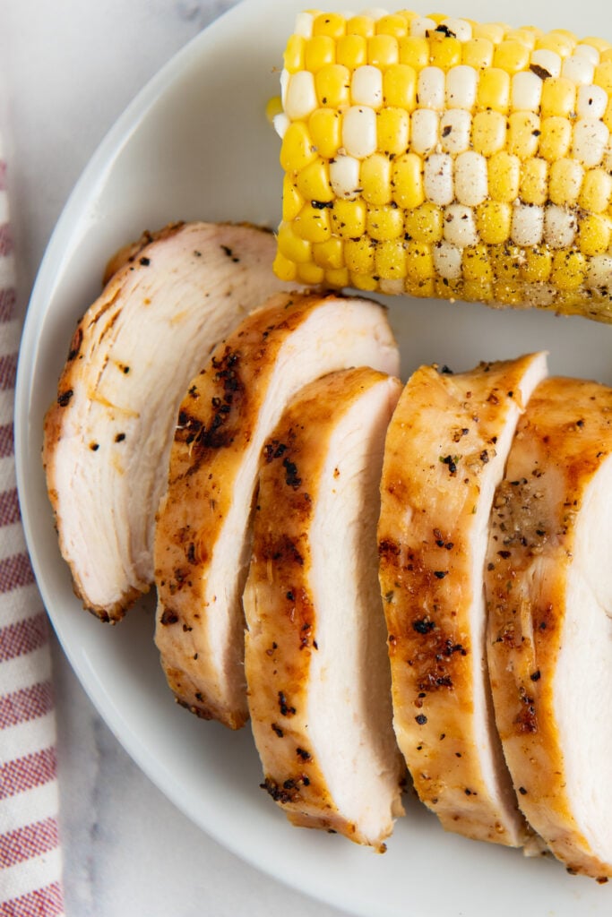 Cut grilled chicken on a white plate with corn on the cob
