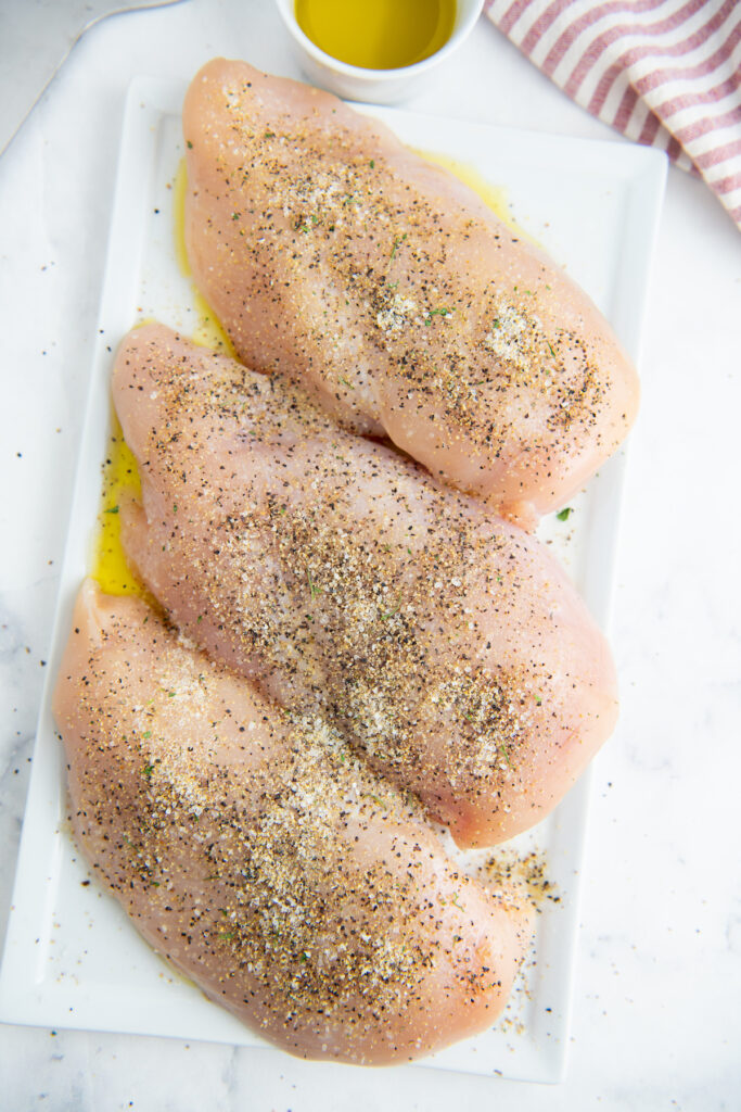 Raw chicken with seasonings on a white tray.