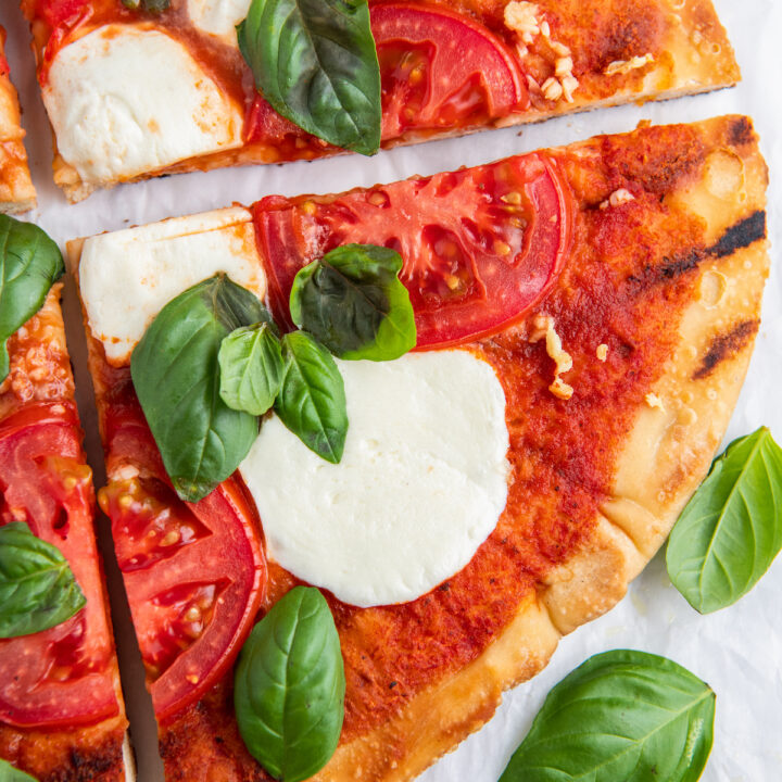 A slice of grilled margherita pizza with fresh basil