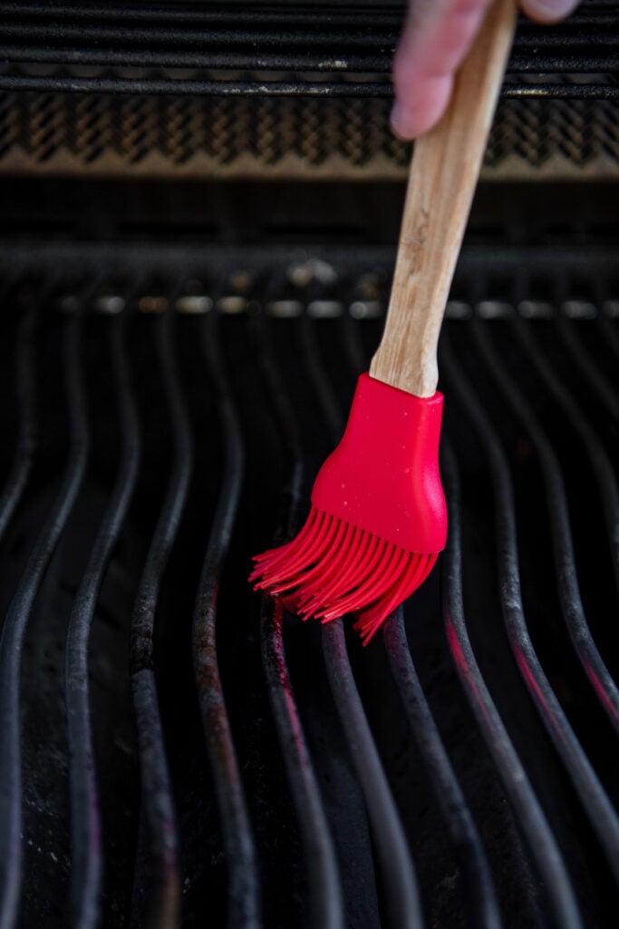 Gas grill with a red basting brush applying olive oil to the grate