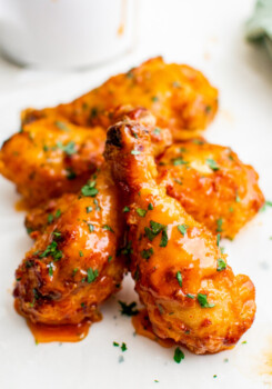 A serving of hot honey wings are on a white surface with sauce in the background.