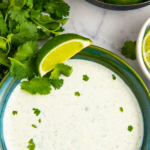 Cilantro cream sauce in a green bowl with lime wedges and fresh cilantro