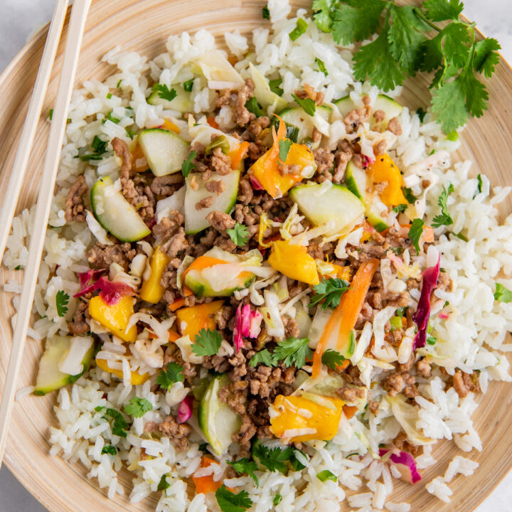 A serving of rice, meat and veggies is presented on a tan plate.