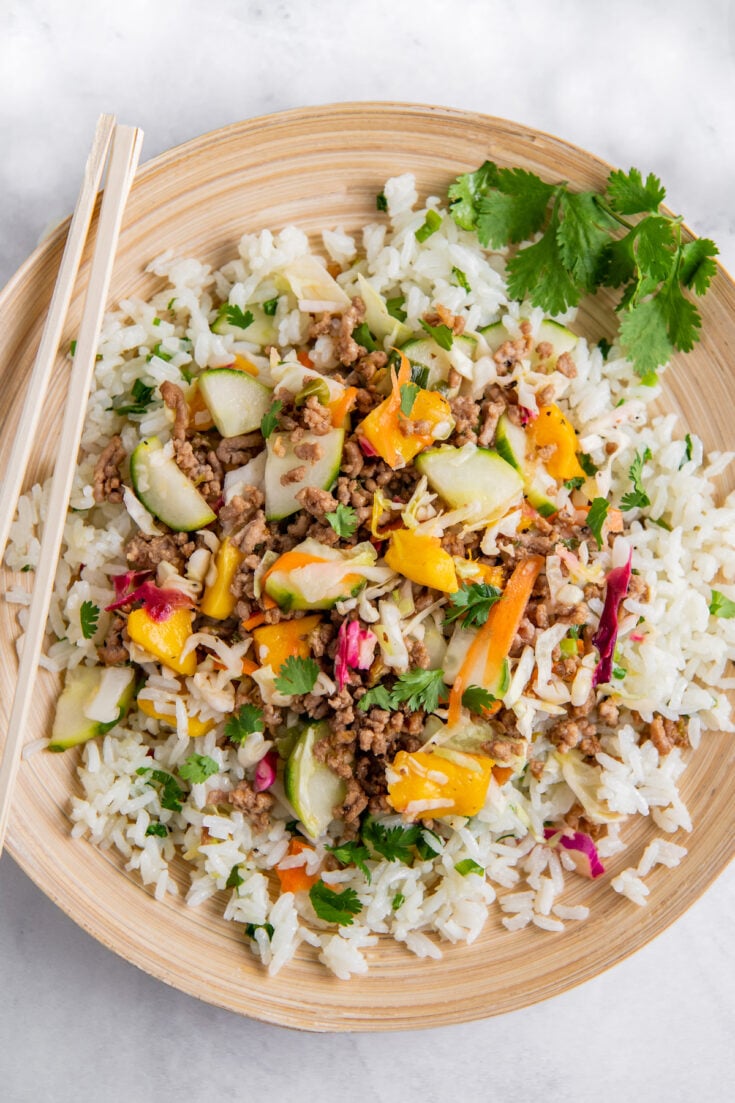 A serving of rice, meat and veggies is presented on a tan plate.