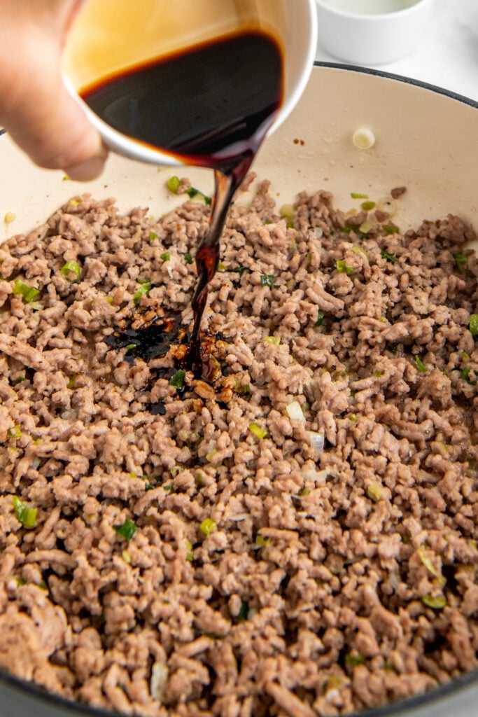 Soy sauce is being poured onto brown ground meat. 