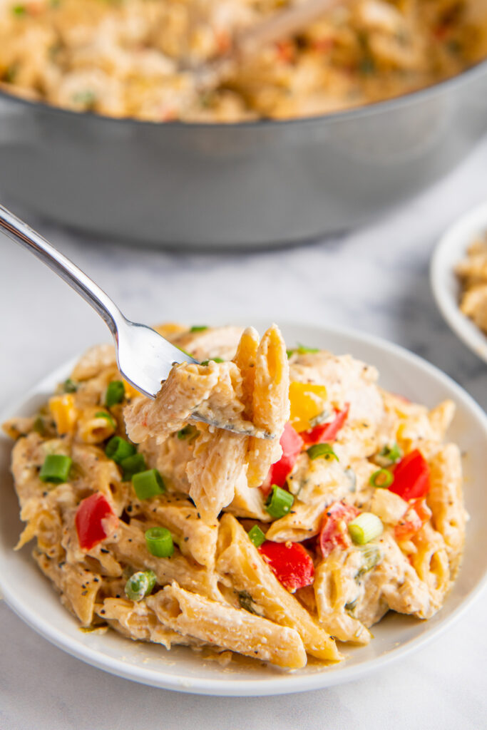 A bite of pasta is being lifted by a fork from a full white plate.