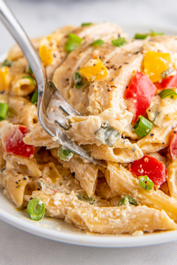 A fork is lifting a bite of pasta from the full plate.