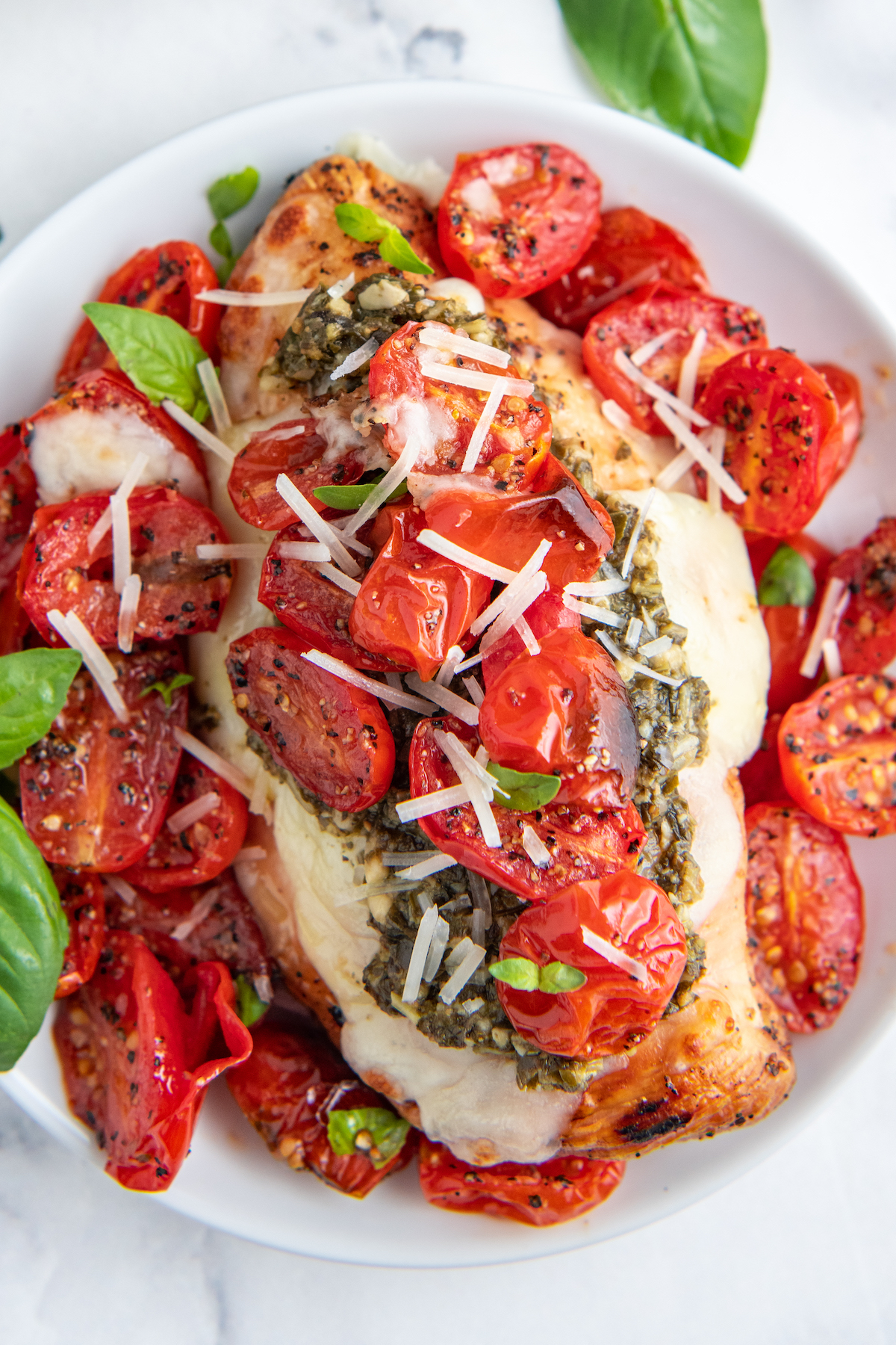 Tomatoes and grilled chicken are topped with shredded cheese.