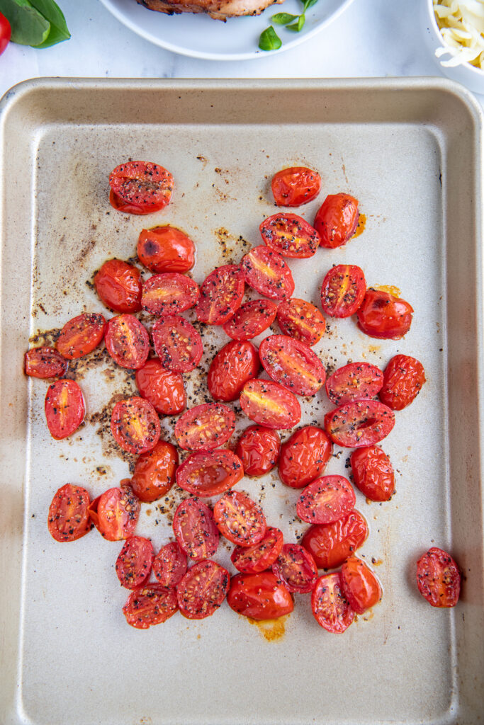 Roasted cherry tomatoes are on a baking sheet. 