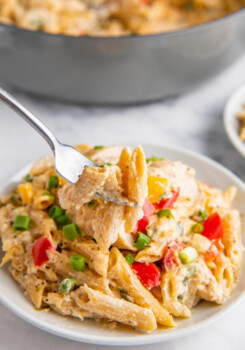 A bite of pasta is being lifted by a fork from a full white plate.