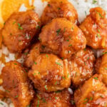 Overhead image of orange chicken served over rice with an orange wedge.