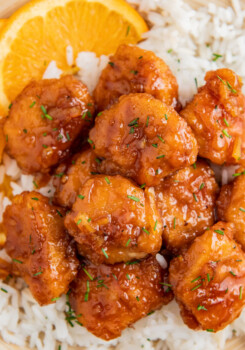 Overhead image of orange chicken served over rice with an orange wedge.