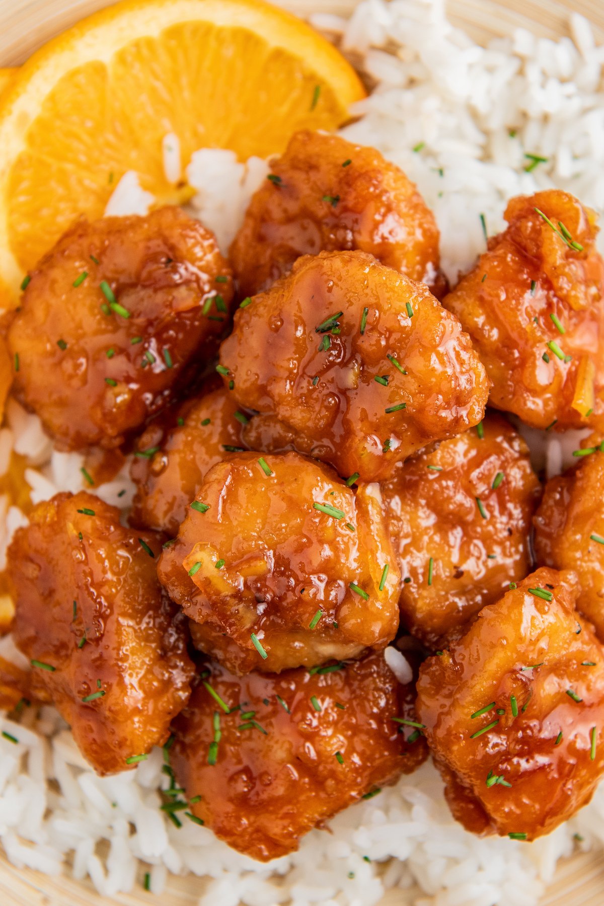 Overhead image of orange chicken served over rice with an orange wedge. 