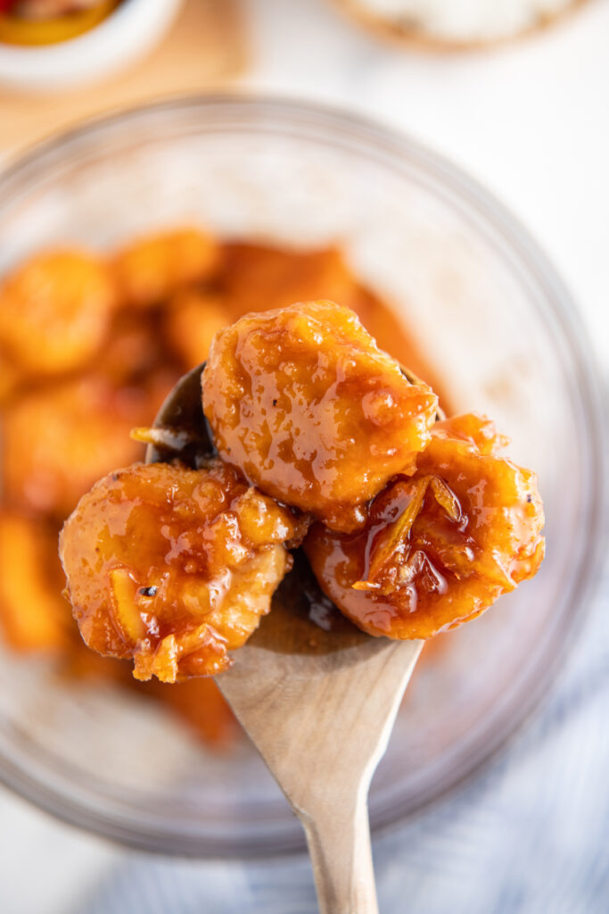 Orange chicken on a wooden spoon with orange sauce on it. 