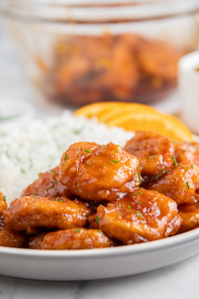 Air fryer orange chicken on a white plate with rice behind it. 