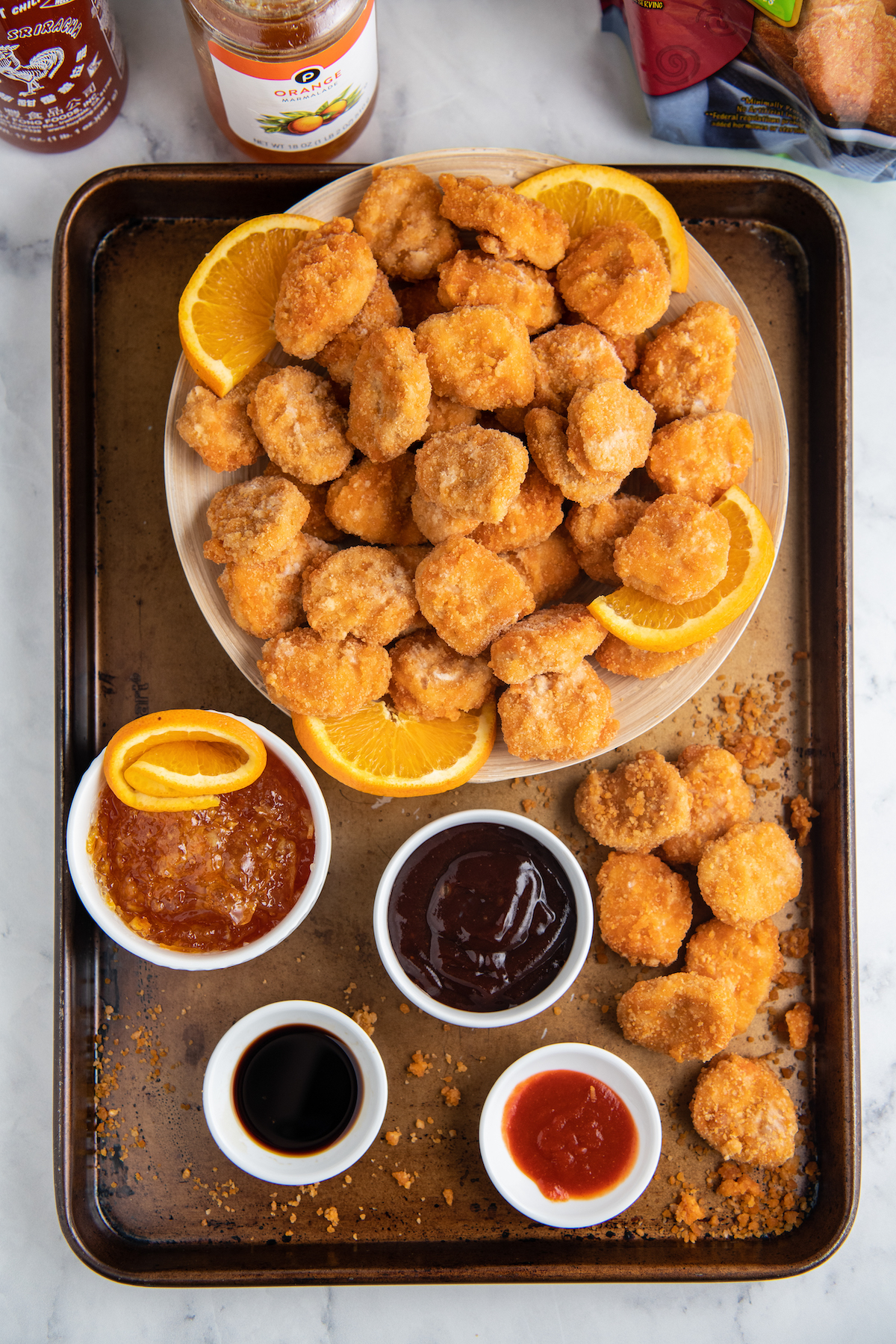 Chicken nuggets in a bowl with a sheet pan under holding the sauces in bowls. 