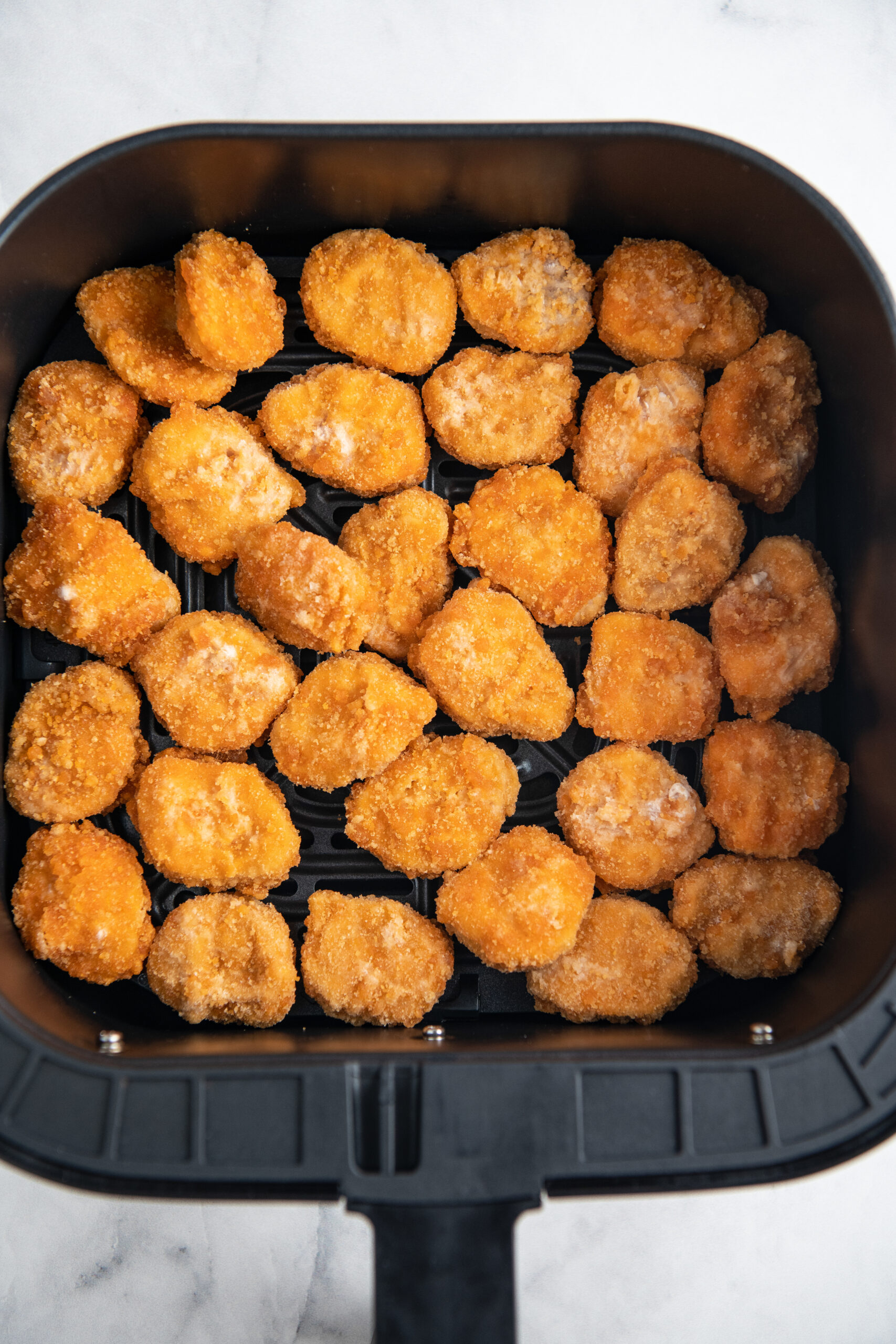 Overhead image of frozen chicken nuggets in an air fryer basket.