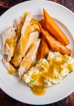 Up close image of turkey breast with gravy, mashed potatoes and carrots on a white plate.