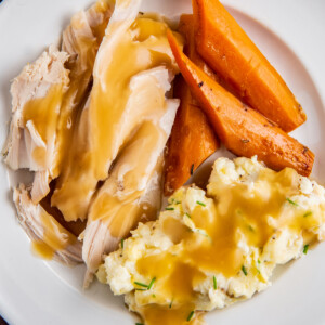 Up close image of turkey breast with gravy, mashed potatoes and carrots on a white plate.