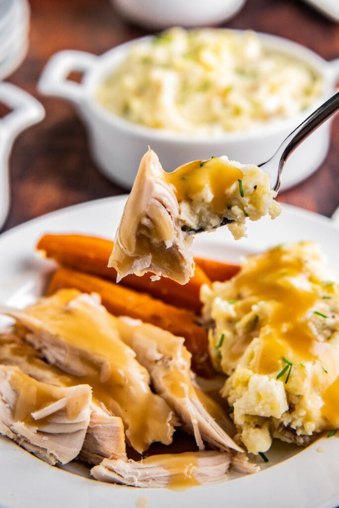 A forkful of turkey and mashed potatoes with gravy on them.