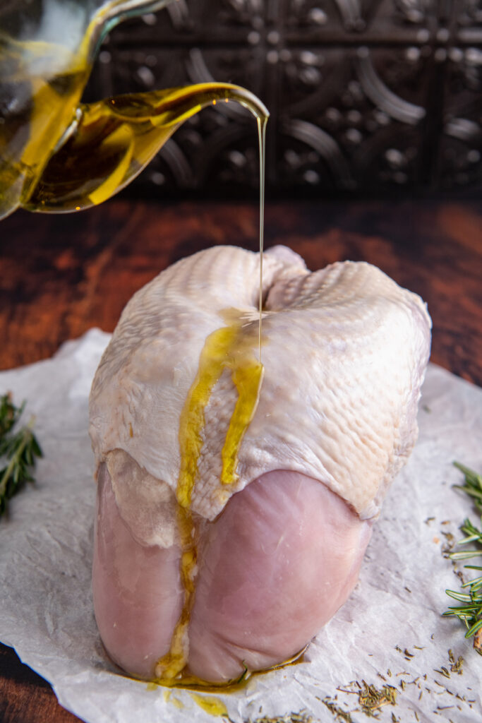 Turkey breast on parchment paper with olive oil drizzled on top.