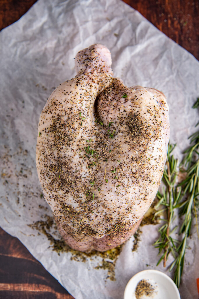 Overhead image of raw turkey breast with seasonings on it set on parchment paper.