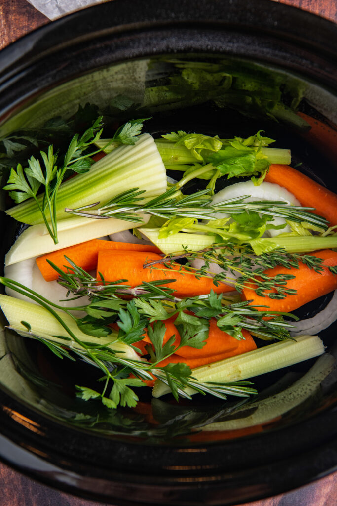 Herbs and carrots added to a crockpot insert.