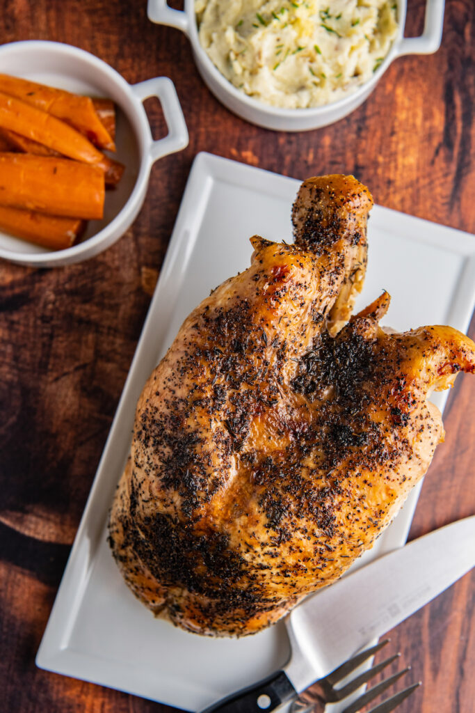 Overhead image of a whole crooked turkey breast about to be carved with a large knife.