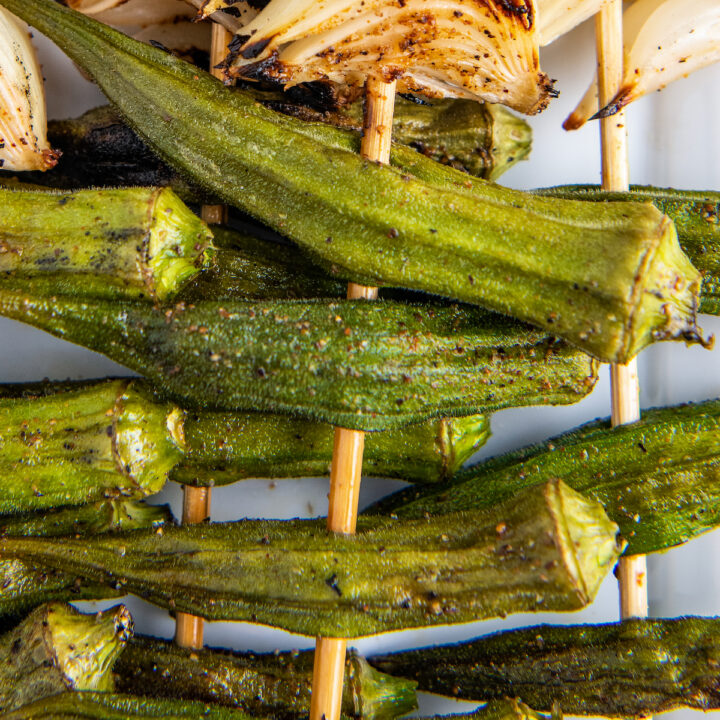 Overhead image of grilled okra with seasonings on it on a skewer with onion.