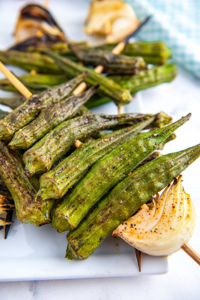 Grilled okra with seasonings on it on a skewer with onion.