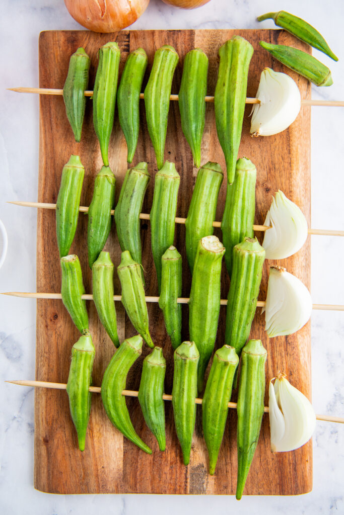 Okra on skewers with onion on a cutting board.
