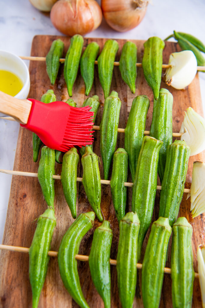 Okra on skewers being brushed with olive oil.