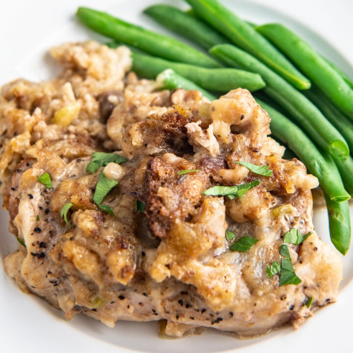 Up close image of slow cooker pork chops on a white plate with stuffing on top and green beans on the side.