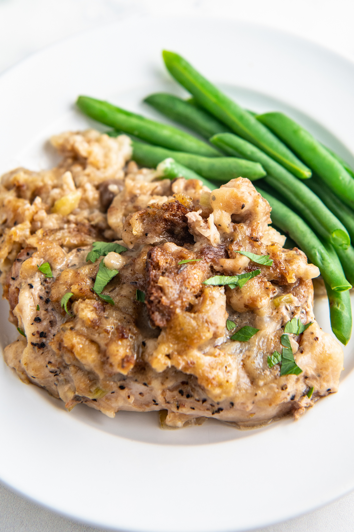 Up close image of slow cooker pork chops on a white plate with stuffing on top and green beans on the side.