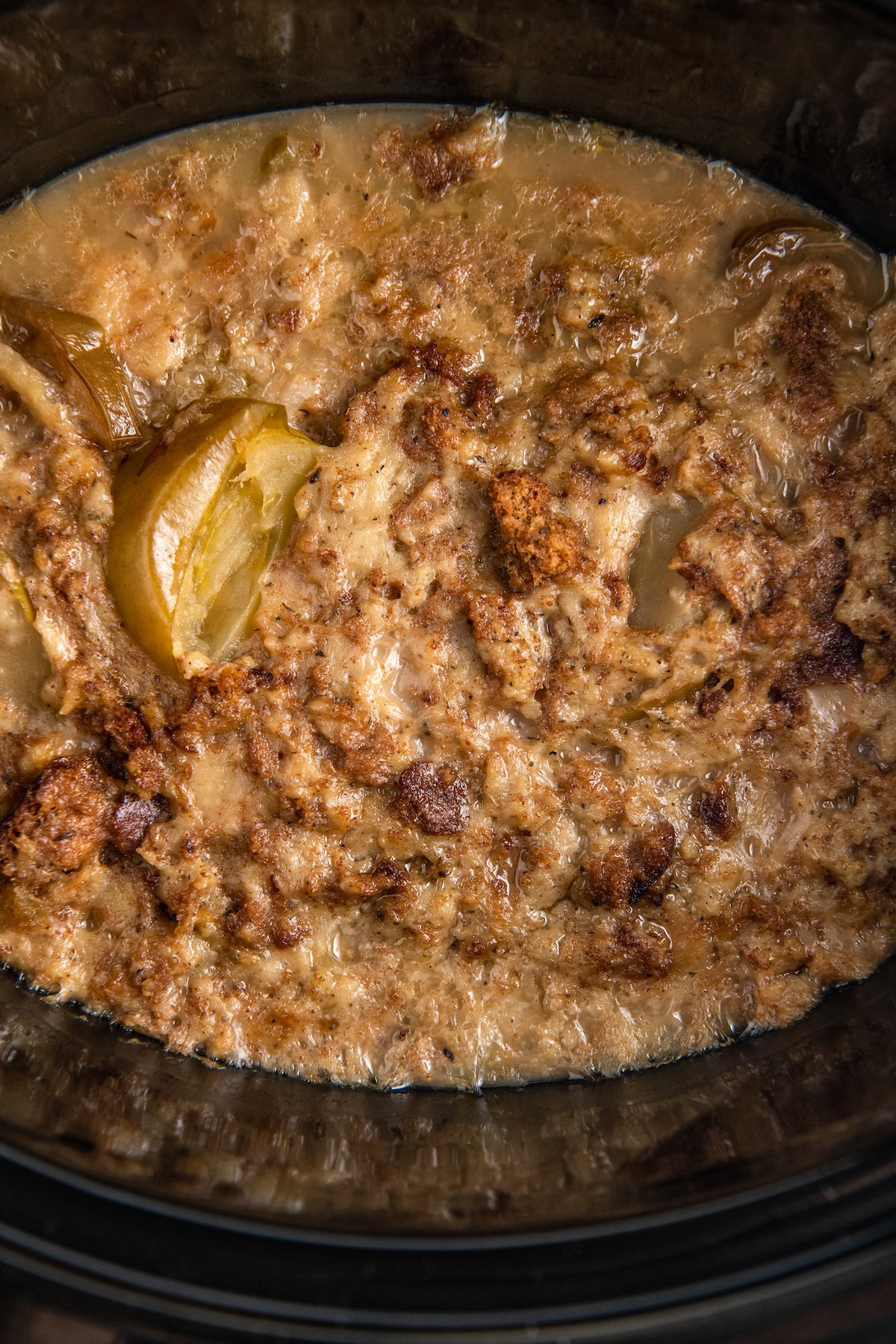 Overhead image of cooked stuffing on top of pork chops with gravy in a crockpot. 