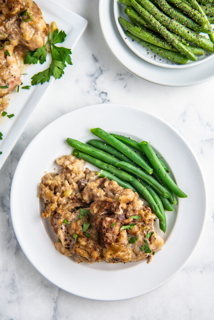 serving plate with green beans and pork chops and stuffing laid out with a side of just green beans in the background
