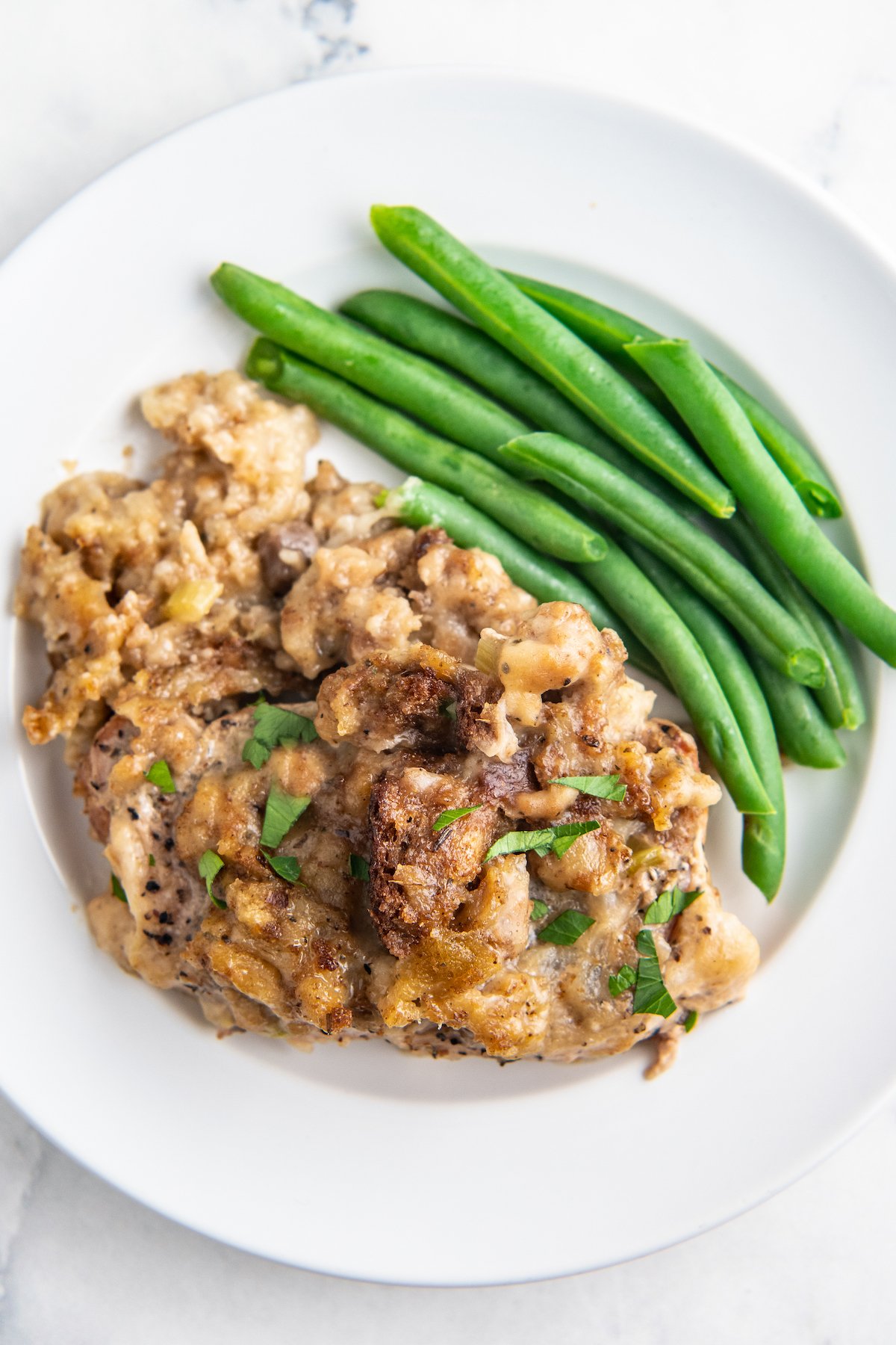 Overhead image of pork chop with stuffing on a white plate with green beans. 