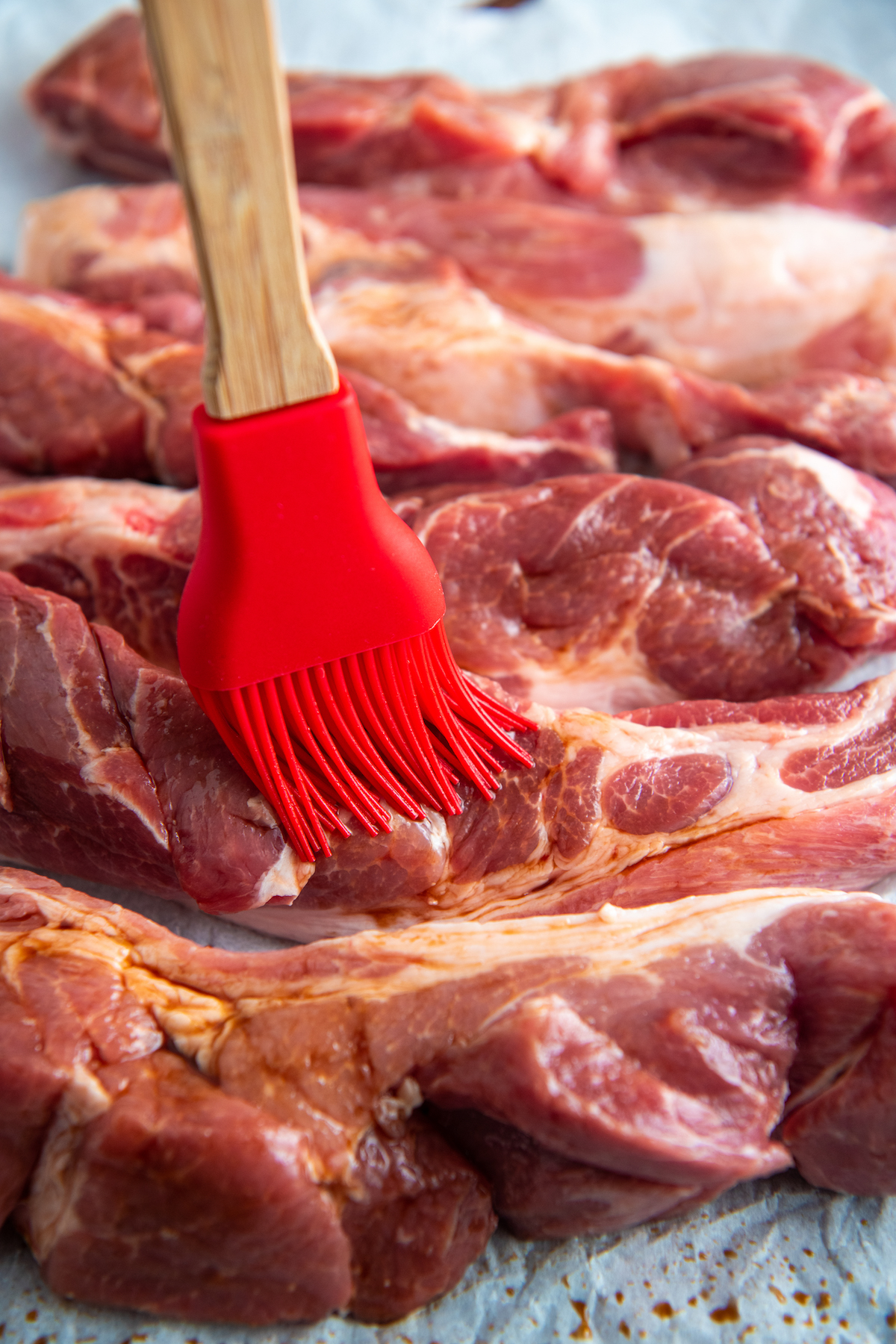 red pastry brush adding oil to boneless ribs